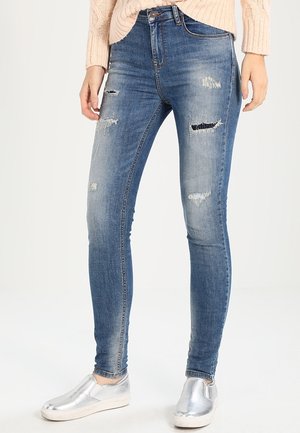 Blå slitna skinny jeans med fransade lappar, med en mid-rise midja och ljus blekning. Kombineras med silverfärgade slip-on skor.