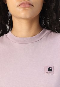 Svijetloplav majica od pamuka s rebrastim okruglim izrezom i malim crnim logom u zakrivljenom dizajnu na lijevoj strani prsiju.