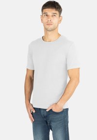 Graziles, kurzärmliges T-Shirt mit Rundhalsausschnitt, sanfter Textur und einem dezenten Logo auf der Brust, kombiniert mit blauen Jeans.