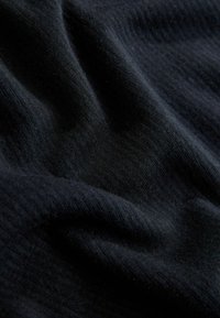 Tessuto nero con una texture morbida e a coste, caratterizzato da pieghe e piegature delicate che mettono in risalto le sue caratteristiche di leggerezza ed elasticità.