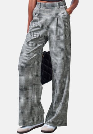 Person wearing high-waist gray plaid wide-leg trousers, white sneakers, and a gold bracelet, holding a black quilted handbag.