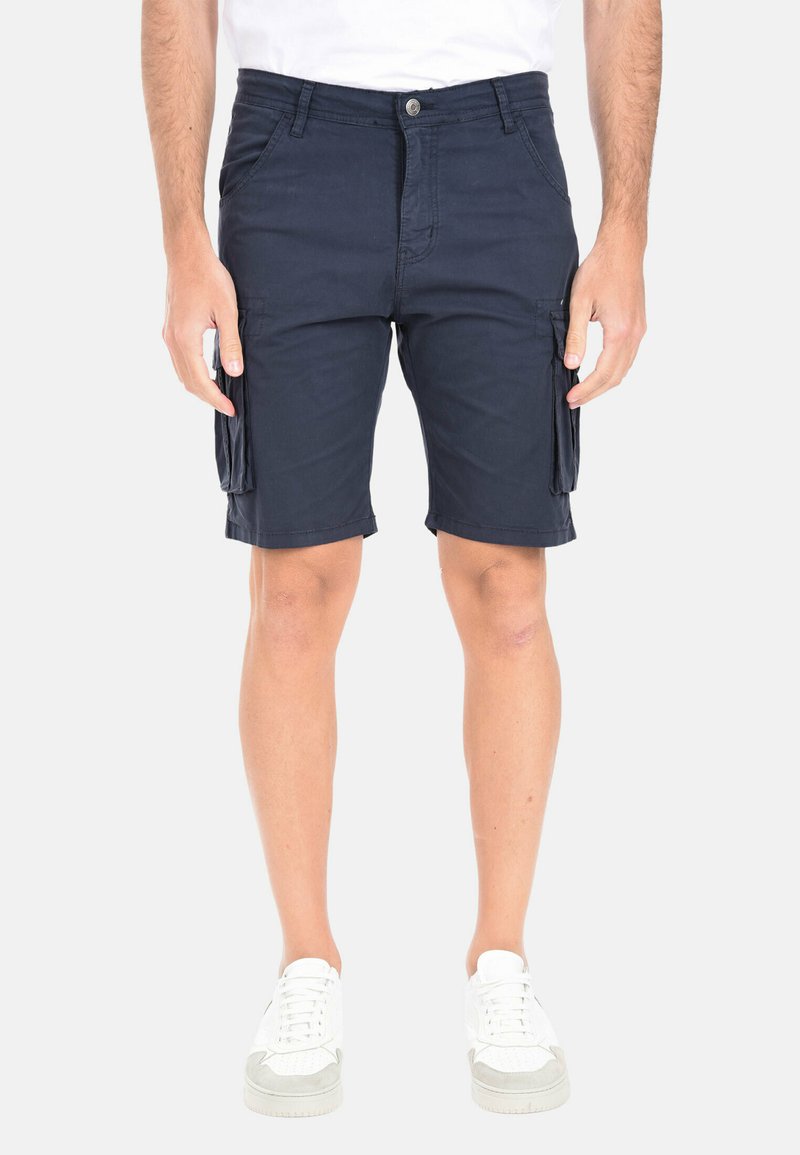 Pantaloni cargo blu navy in cotone, con numerose tasche, taglio dritto e dettagli cuciti. Indossati con sneakers bianche.