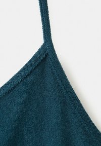 Zbliżenie na ciemnoturkusową tkaninę frotte z cienkim paskiem i ukośnym detalem szwu.