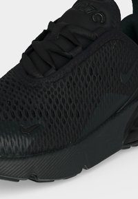 Gros plan d'une chaussure de sport noire texturée avec une tige en mesh, une fermeture à lacets et des logos Nike Swoosh discrets sur le côté et la pointe.