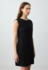 Schwarzes ärmelloses Kleid mit rundem Ausschnitt, tailliertem Schnitt, glatter Textur und knielanger Silhouette. Minimalistisches Design, keine Muster.