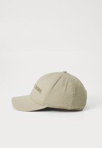 Khaki värvi pesapalli müts, millel on kõver sirge, pruunist broderinguga logo, kuue paneeliga disain ja ventilatsiooni augud külgedel.