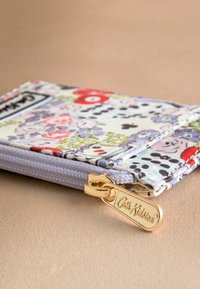 Gėlių rašto piniginė, pagaminta iš audinio, su violetiniu užtrauktuku. Ji turi auksinį užtrauktuko traukiklį su išgraviruotu „Cath Kidston“ užrašu.