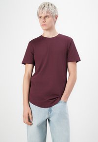 Burgunderfarbener T-Shirt mit kurzen Ärmeln aus weichem Baumwollmaterial, mit Rundhalsausschnitt und lockerer Passform, kombiniert mit hellblauen Jeans.
