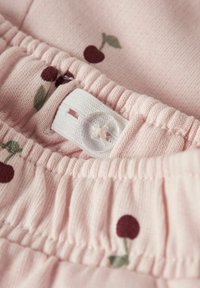 Różowa tkanina z elastycznym paskiem w talii, z regulowanym otworem na guzik oraz szczegółami w postaci wiśni w ciemnoczerwonym i zielonym kolorze.