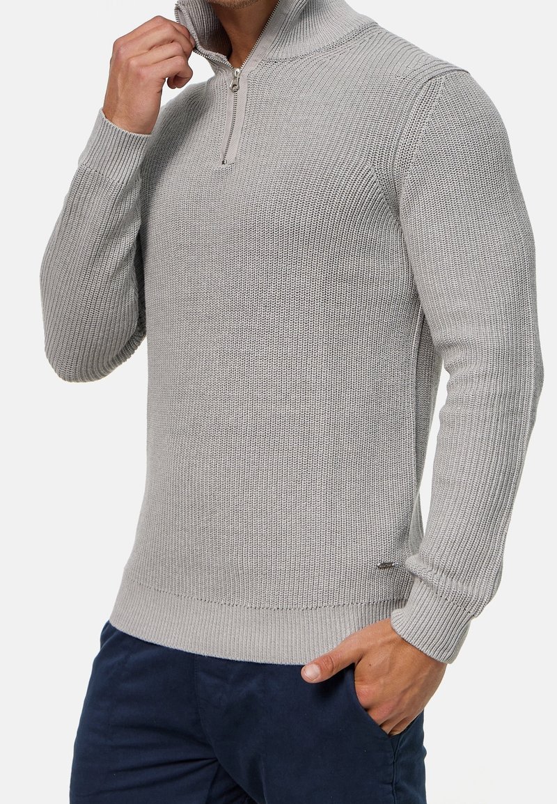 Lichtgrijze gebreide trui met een halve rits kraag, voorzien van getextureerde ribbelstof en aansluitende mouwen, gecombineerd met donkerblauwe broek.
