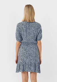 Robe à manches courtes de couleur bleu clair avec un motif à taches noires. Présente une taille smockée et un ourlet volantr. Texture de tissu lisse.