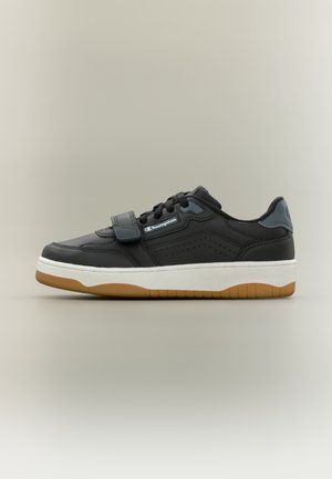 Sort lædersneaker med en hvid mellemsål og brun gummiydersål. Har en velcrolukning og perforerede detaljer på siderne.