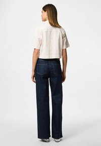 Camicia accorciata a maniche corte in un tenue colore pastello con motivo sottile; abbinata a jeans in denim scuro a vita alta e gamba larga.