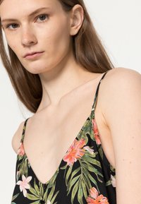 Vestido preto com padrão floral, apresentando grandes flores rosa e brancas com folhas verdes, alças finas e um decote em V profundo com detalhe de botões.