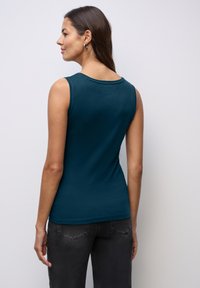 Top senza maniche di colore teal con collo rotondo, realizzato in tessuto morbido. Sottile e aderente, con una texture liscia e senza motivi o accessori visibili.