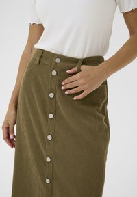 Olive green corduroy skirt with a high waist, featuring a row of silver buttons down the front and side pockets. Textured fabric visible.