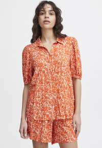 Orange button-up shirt and matching shorts with a floral pattern. Short puff sleeves, lightweight fabric, and a relaxed fit design.