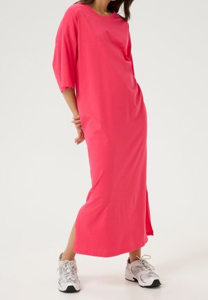 Robe maxi en coton rose avec manches courtes, fentes latérales et coupe décontractée, associée à des baskets athlétiques blanches et grises.