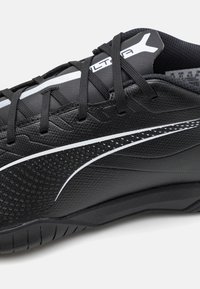 Sneakers atletici neri con tomaia sintetica testurizzata, accenti bianchi, lacci piatti e suola curva per flessibilità.