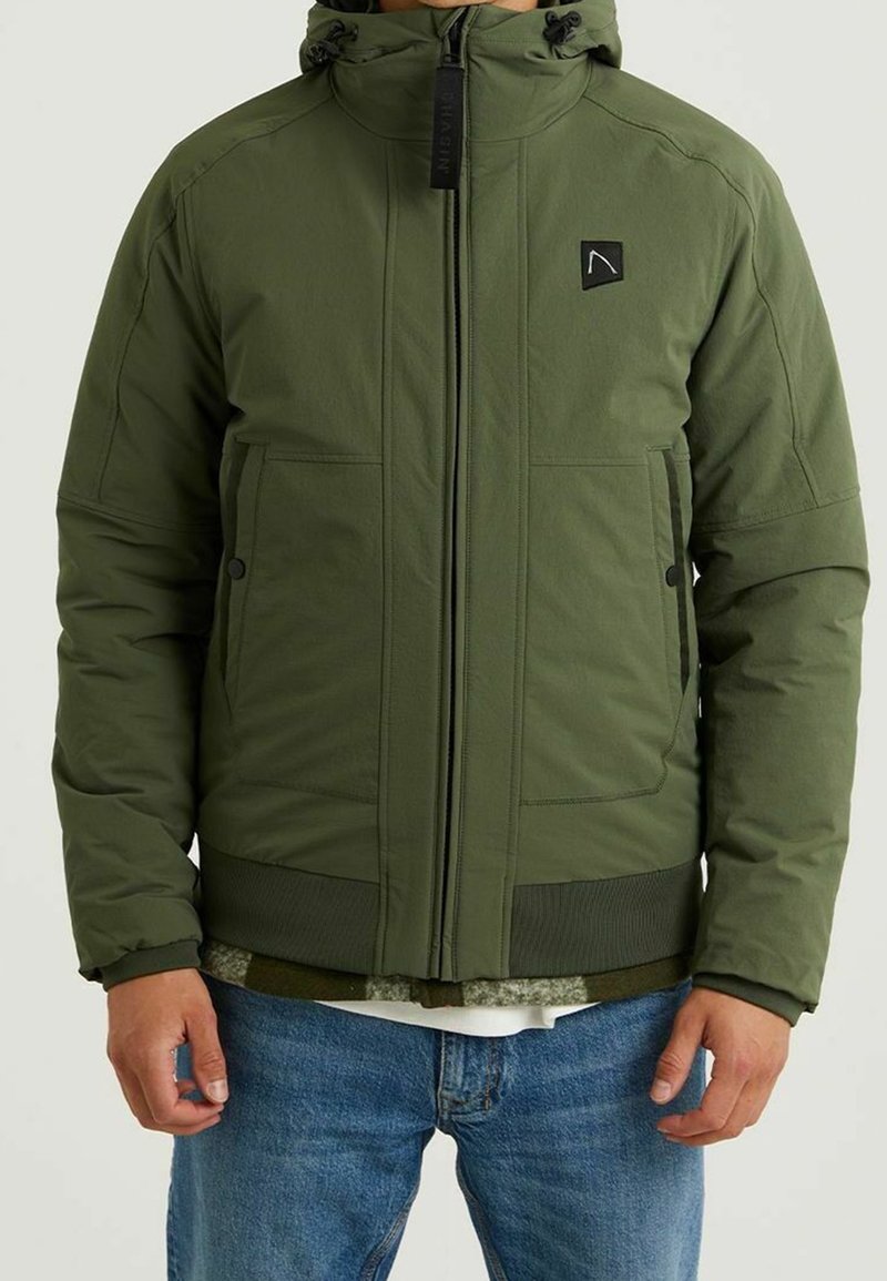 Zelená péřová bunda s kapucí, zipovým zapínáním, dvěma postranními kapsami, žebrovaným lemem a černou nášivkou na levém prsu. Materiál vypadá texturovaně.