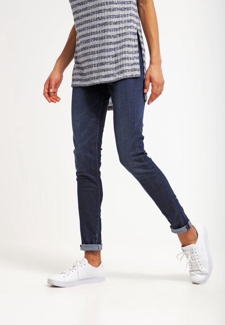Smal blå denimjeans med lätt stretch, med uppvikta benslut och parat med vita sneakers. Modell som bär en mönstrad topp.