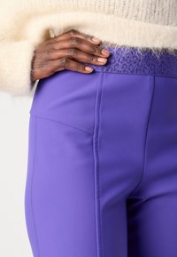 Paarse leggings met een textuurrand en een subtiele luipaardprint. Gemaakt van soepel materiaal met een aansluitende pasvorm en een zijzak.