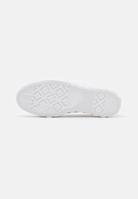 Semelle de basket blanche avec des motifs de grip texturés comprenant des losanges, des lignes et des formes croisées, présentée sur un fond blanc uni.