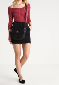 Top rosso scollato su un spalla con maniche a tre quarti, abbinato a una gonna di jeans nera e a una piccola borsa a tracolla nera. Scarpe nere basse.