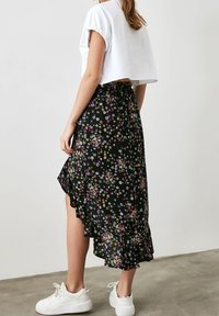 Černá květinová sukně s fialovými, bílými a žlutými květy, s volánkovým lemem. Kombinováno s krátkou bílou košilí a bílými teniskami.