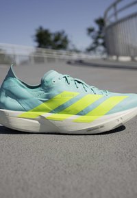 Lyseblå løbesko med lysegule striber og en hvid sål mærket Lightstrike Pro på en betonoverflade udendørs.