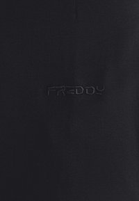 Camiseta de tela negra con una textura suave y un sutil logotipo bordado de "FREDDY". Diseño sencillo con un cuello clásico y sin patrones adicionales.