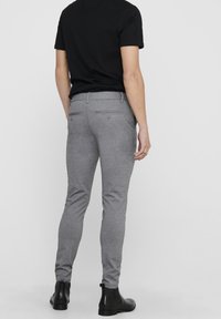 Grijze slim-fit broek met een gladde textuur, voorzien van achterzakken en zijnaden, gecombineerd met een zwart shirt met korte mouwen en enkelboots.