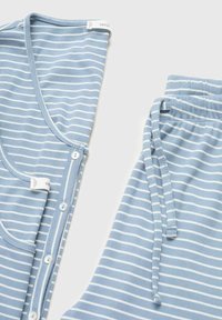 Set pentru bebeluși format dintr-un salopetă cu dungi albastre și albe și o pereche de pantaloni. Salopeta are nasturi, iar pantalonii dispun de un șnur de ajustare.