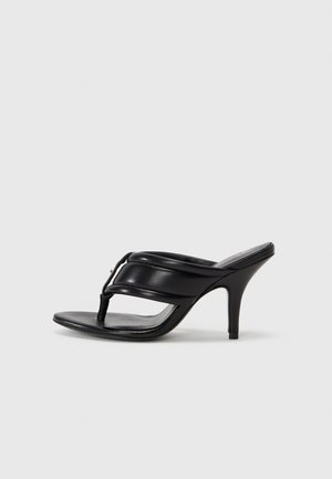 Juodos odinės aukštakulnės šlepetės su plona juostele ir pirštų postūmiu. Lygus paviršius, smailas padas ir liekna stiletto kulnas.