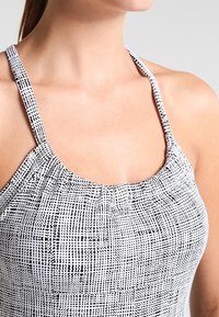 Černobílé vzorované plavky s nabíraným výstřihem do půlkruhu a tenkými ramínky. Materiál působí lehce a má hladkou texturu.