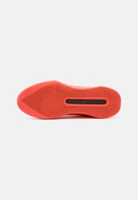 Semelle d'une chaussure de sport rouge avec des motifs de bande de roulement circulaires et triangulaires et un détail ovale noir au centre.