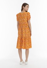 Oranges Blumenkleid mit Puffärmeln, gestuftem Saum und lockerer Passform. Es hat ein florales Muster in Rosa, Weiß und Grün vor einem hellen Hintergrund.