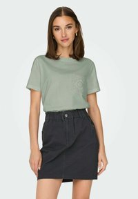 Lys grøn bomuld t-shirt med tekstureret lomme detaljer og sort denim nederdel med elastisk talje og sidelommer.