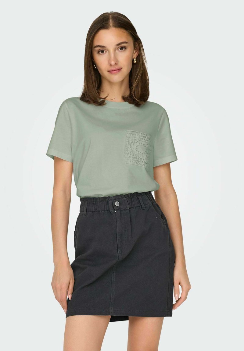 Lys grøn bomuld t-shirt med tekstureret lomme detaljer og sort denim nederdel med elastisk talje og sidelommer.