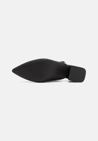 Black pointed-toe shoe with a smooth leather upper, textured sole, and a block heel. The sole features a rubberized grip for traction.