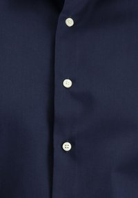 Granatowa koszula o gładkiej fakturze, z siedmioma srebrnymi guzikami z przodu oraz prostym, pozbawionym wzorów i akcentów krojem.