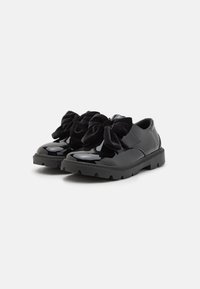 Schwarze Lacklederschuhe mit klobigen Sohlen, die an der Vorderseite große, weiche Samtbows und eine strukturierte Gummisohle für Grip aufweisen.