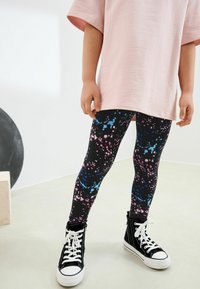 Färgglada leggings med en svart bas och rosa- och blåsprutningsmönster, parat med en lös rosa tröja och svarta högstövlar.