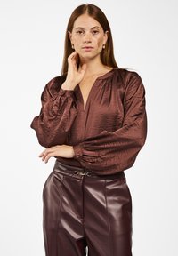 Bruine satijnen blouse met een diepe V-hals, poffende lange mouwen en knoopsluiting bij de manchetten, gecombineerd met hooggewaisted donkerburgundy neplederen broek.
