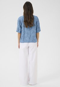 Svetlo modra kratka majica s teksturiranim vzorcem, kombinirana z belimi širokimi hlačami, ki imajo sproščeno prileganje in mehak material.