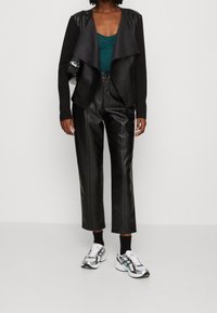 Schwarze Kunstlederjacke mit drapiertem Vorderteil, türkisfarbener Spitzenoberteil und schwarze Kunstlederhose. Weiße und silberne Sportsneaker runden den Look ab.