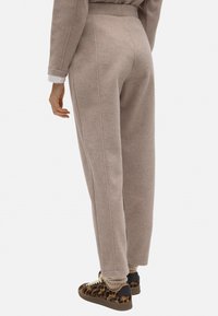 Joggers de felpa marrón claro con un corte ajustado, que cuentan con costuras laterales y cintura con cordón. Combinados con zapatillas de deporte con estampado.