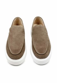 Bruine suede instappers met een gladde textuur, een verlengd punt, en een witte rubberen zool, met een minimale stitching langs de randen.