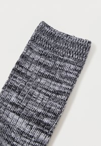 Ponožka čierno-sivých pásikov z pleteného materiálu, s rebrovaným zúžením a textúrovaným povrchom.