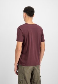 Burgunderfarbenes T-Shirt mit kurzen Ärmeln und Rundhalsausschnitt, aus weichem Stoff gefertigt, kombiniert mit olivgrünen Cargo-Hosen mit mehreren Taschen.